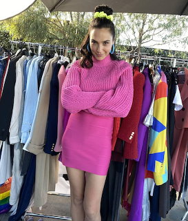 Woman in pink sweater and skirt standing in front of clothing racks outdoors