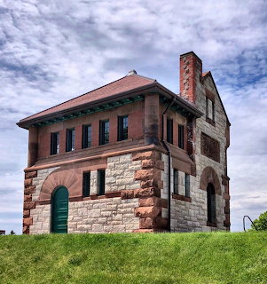 Red brick gatehouse with stone base on green hill under cloudy sky
