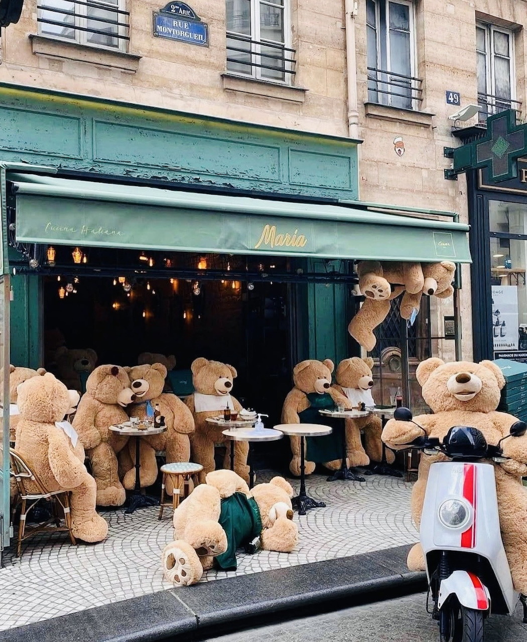 Multiple teddy bears sitting at café tables on a Paris street with buildings in background