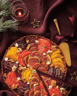 Decorative Christmas tart with colorful fruit slices arranged on burgundy fabric with festive decorations