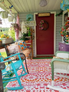 Colorful front porch with red door, turquoise chairs, patterned floor, and hanging plants