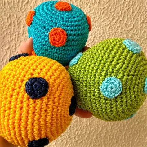 Three crocheted balls in yellow, teal, and green with colorful circle appliqués held in a hand