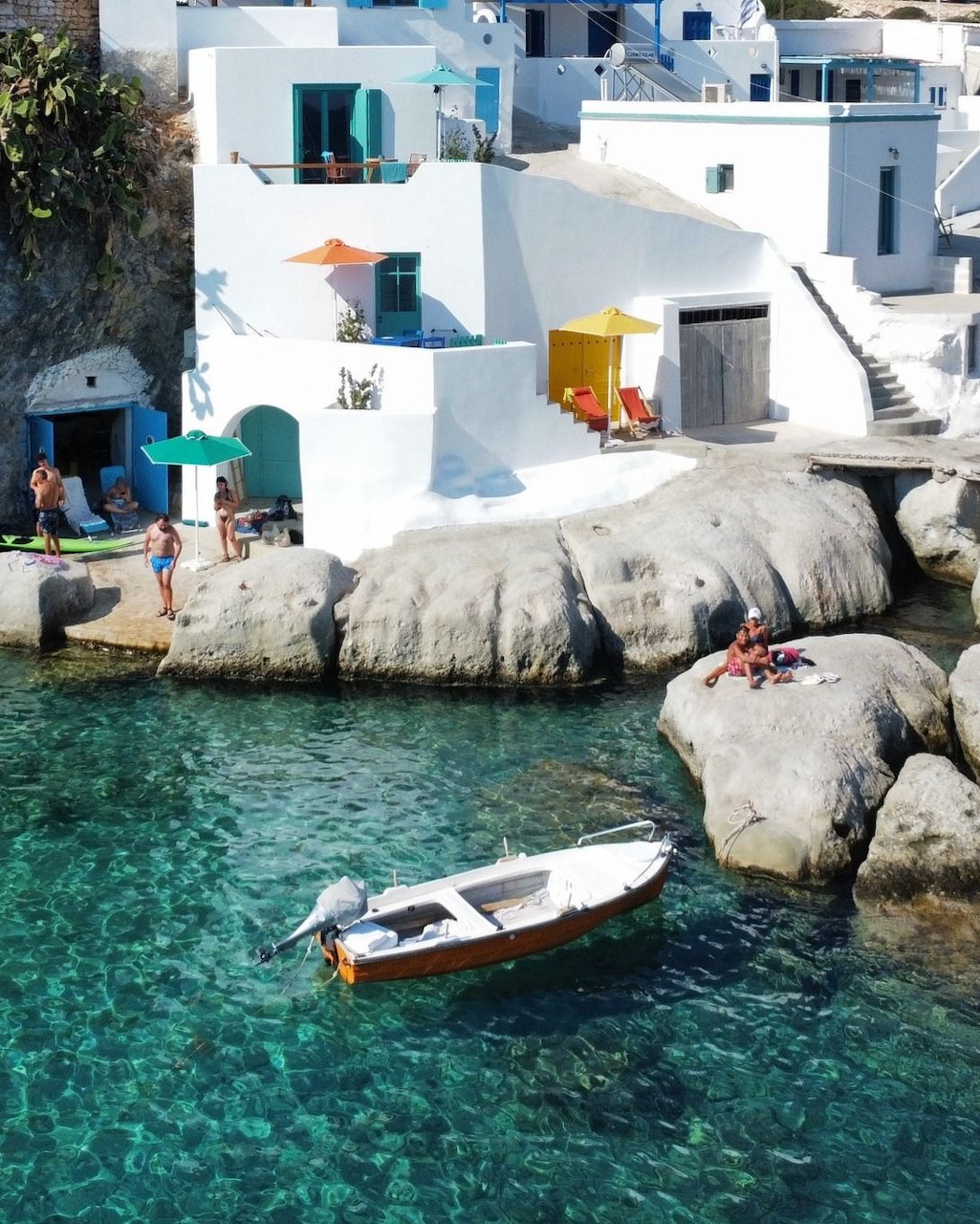 Small boat on turquoise water near white buildings and rocks in Milos, Greece
