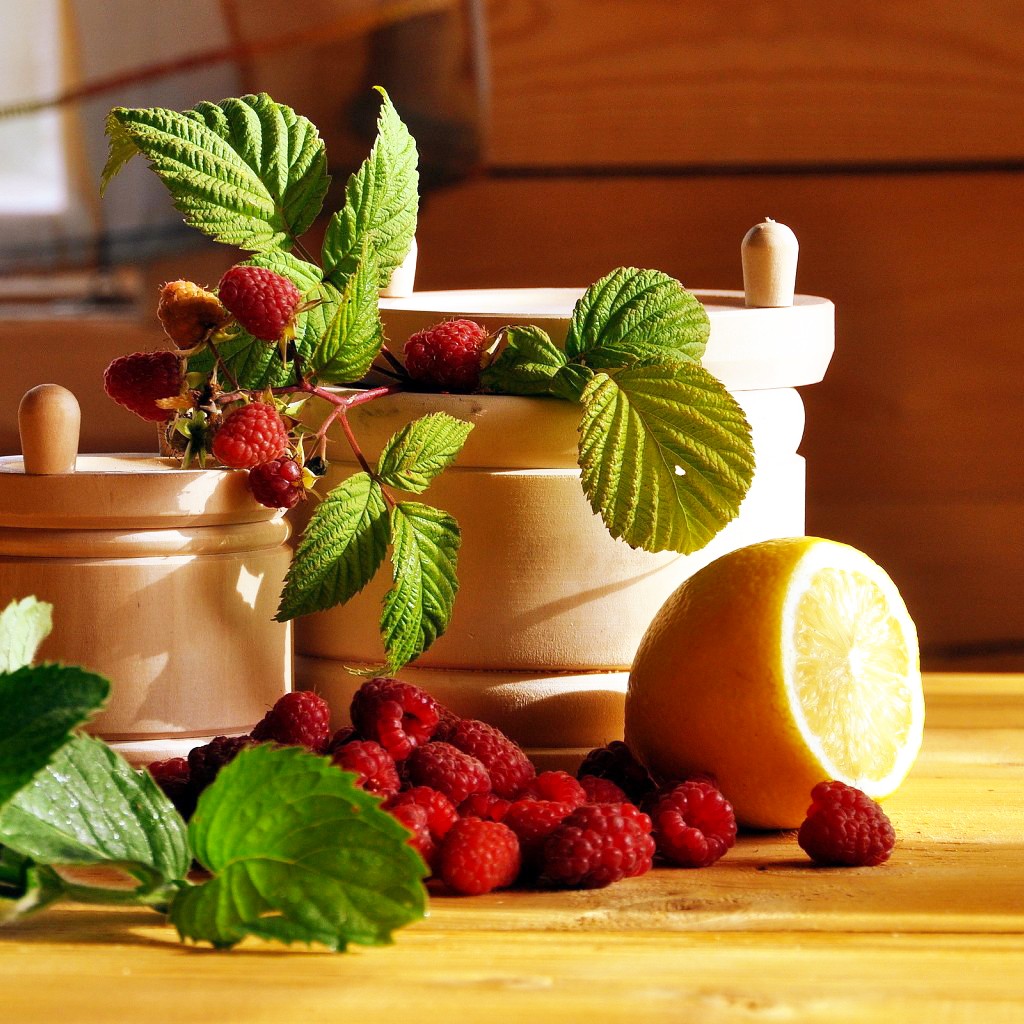 Raspberries with leaves and lemon on wooden table next to white lantern