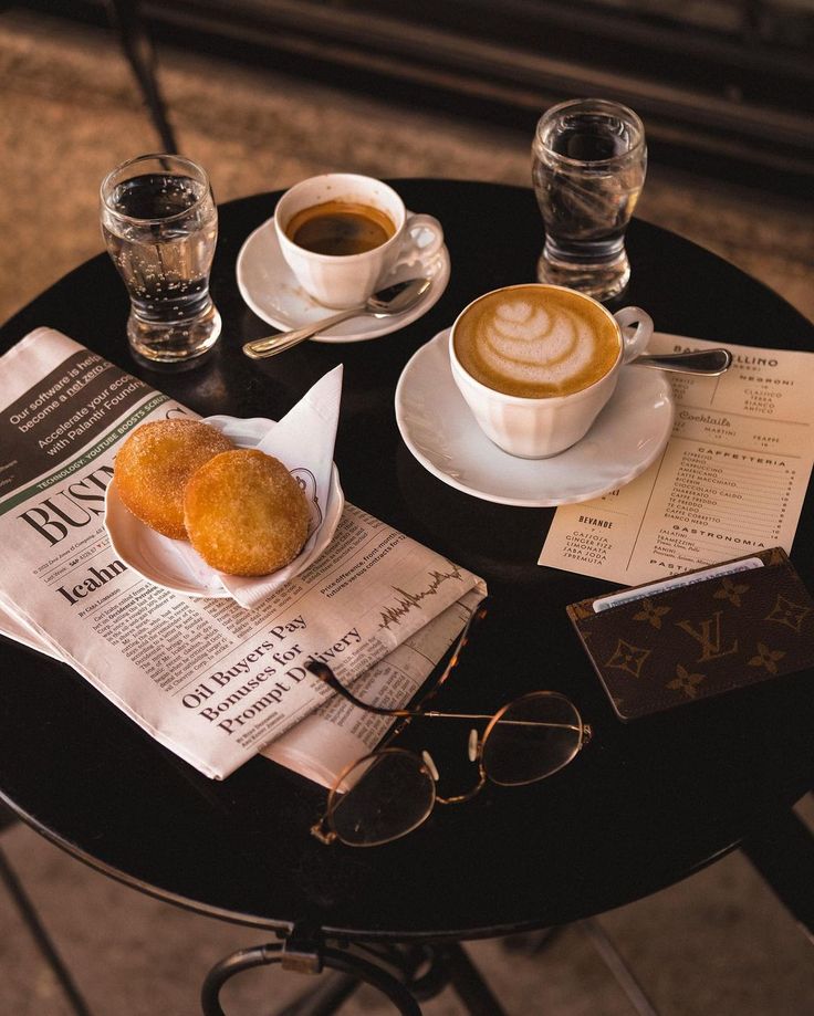 Cup of coffee with latte art next to a dessert and newspaper on a cafe table