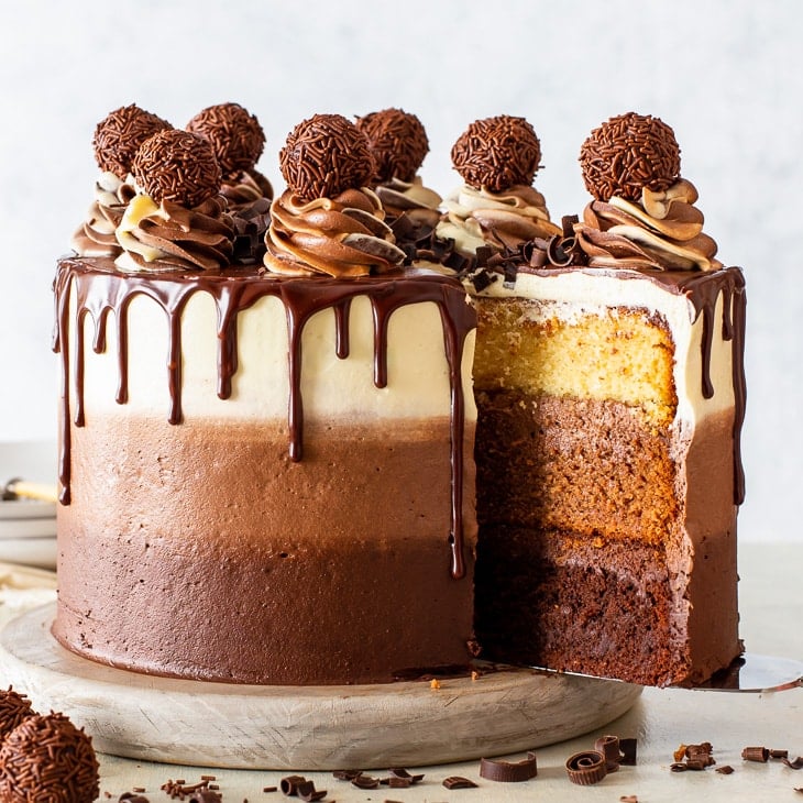 Triple chocolate layer cake with ganache drips, frosting swirls, and a slice cut out
