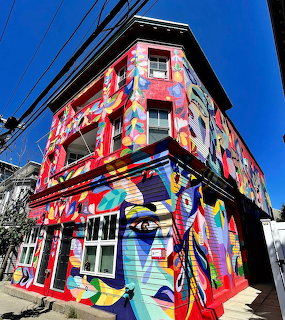 Corner building covered in colorful graffiti murals with bold geometric and abstract designs against blue sky