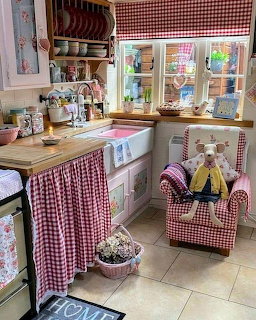 Vintage kitchen with red gingham fabric, white sink, wooden counters, and colorful dishware on open shelves