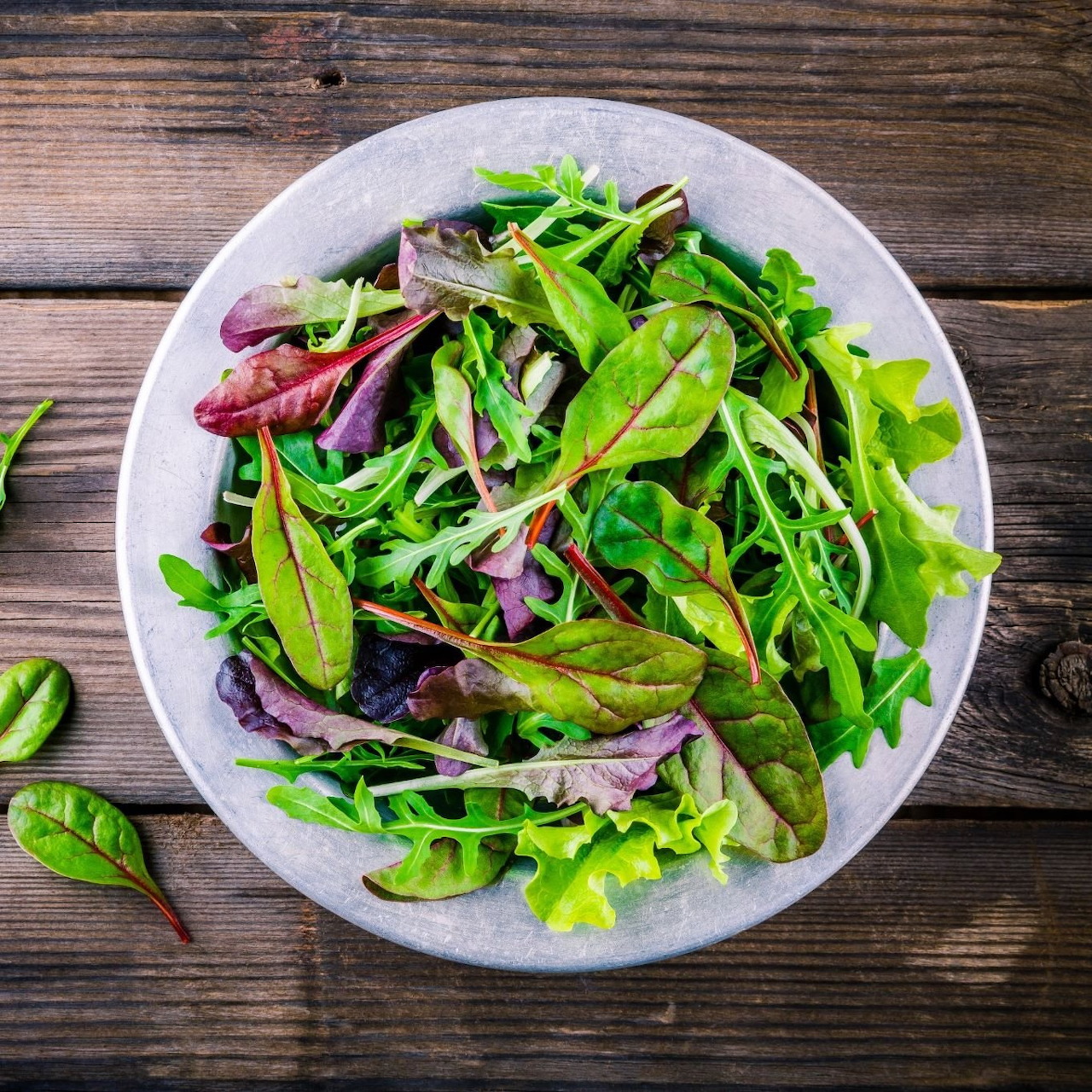 Bowl of fresh mixed green salad leaves on a rustic wooden table