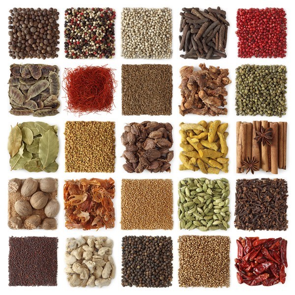 Grid of 25 compartments displaying assorted whole and ground spices including peppercorns, saffron, cloves, and cinnamon