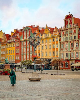 Colorful historic buildings on a cobblestone square in Wroclaw, Poland, with a fountain and lone figure