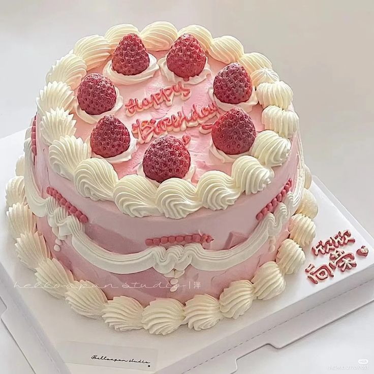 Pink frosted cake topped with strawberries and white whipped cream on a cake board