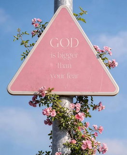 Pink triangular sign with inspirational text surrounded by pink roses against blue sky