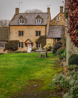Traditional English stone cottage with thatched roof and green lawn garden