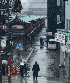 Person walking down rainy Japanese street with traditional buildings and overcast sky