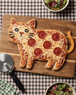Cat-shaped pepperoni pizza on wooden board with pizza cutter and salad bowls
