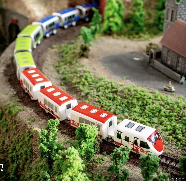 Colorful model passenger train on curved tracks in a miniature village landscape