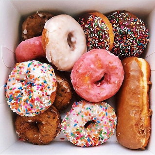 Overhead view of assorted donuts with colorful sprinkles and glazes in a white box