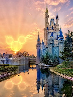 Cinderella Castle with water reflection at sunset showing dramatic orange and purple clouds