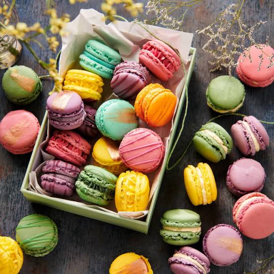 Colorful macarons in a box and scattered on a dark wooden table