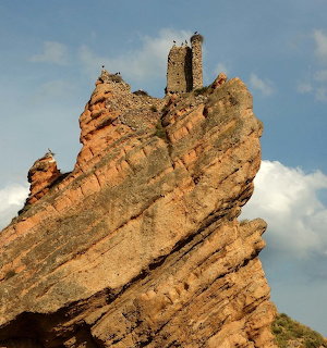 Ruined castle perched on a steep jagged rock formation beneath a blue sky