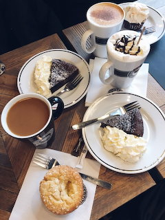 Overhead view of coffee, cake slices with cream, and a pastry on a wooden table