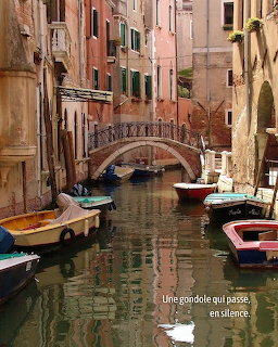 Narrow Venice canal with mored boats, old colorful buildings, and a small arched bridge