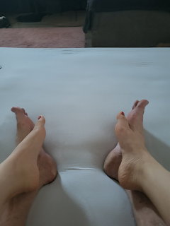 Bare feet resting on a white bed or cushioned surface indoors