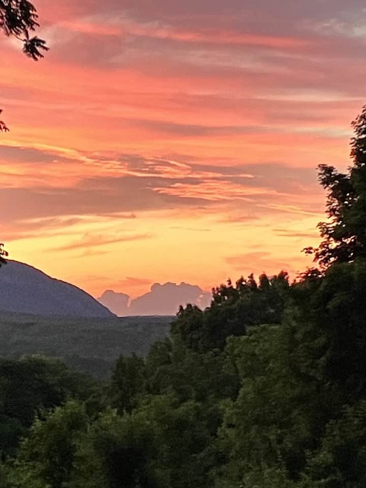 Brilliant orange and pink sunset over mountain ridges with green trees in the foreground