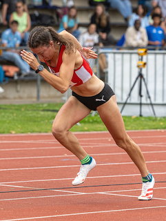 Female sprinter in red top and black shorts launching from the start on a running track