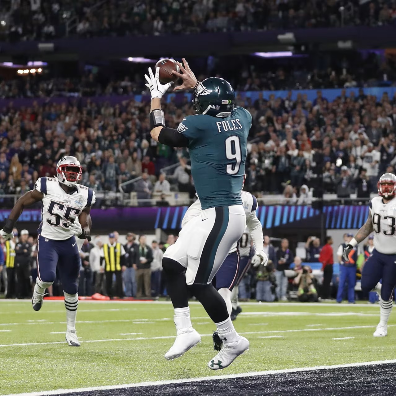 Nick Foles of the Eagles jumping to catch a football during a game as Patriots defenders watch