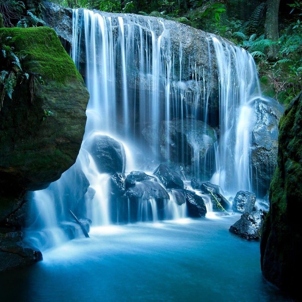 Silky waterfall flowing over mossy rocks into a blue pool in a forest