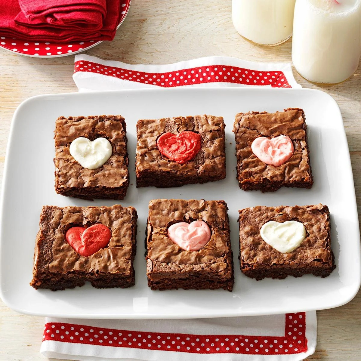 Chocolate brownies with heart decorations on white plate with red ribbon and milk