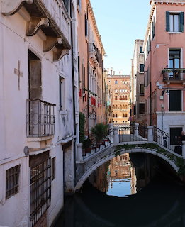 Narrow Venice canal with a stone bridge between old pastel-colored buildings under a clear sky