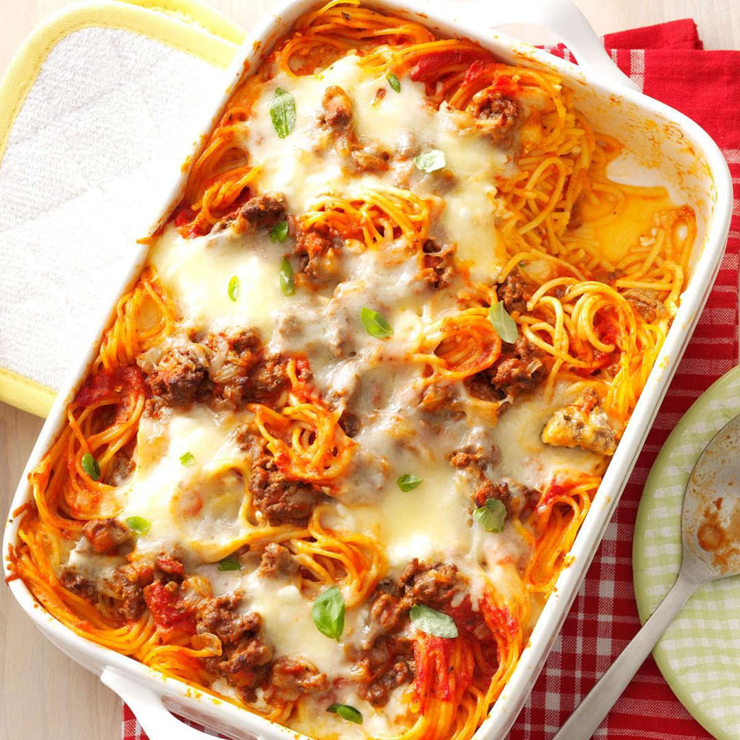 Baked spaghetti casserole with melted cheese and meat in white dish