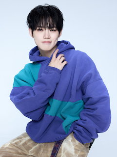 Young man in purple and teal color-block hoodie posing against pale blue background