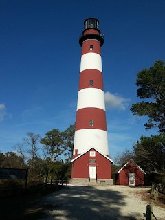 Red and white striped lighthouse beside small red buildings under a blue sky