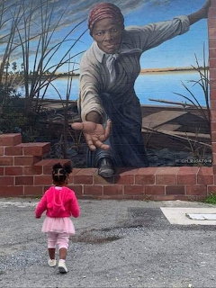 Child viewing large Harriet Tubman mural painted on brick wall showing her with extended arm against water landscape