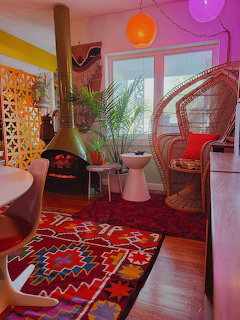 Colorful bohemian interior with patterned rugs, wicker peacock chair, hanging fireplace, and houseplants