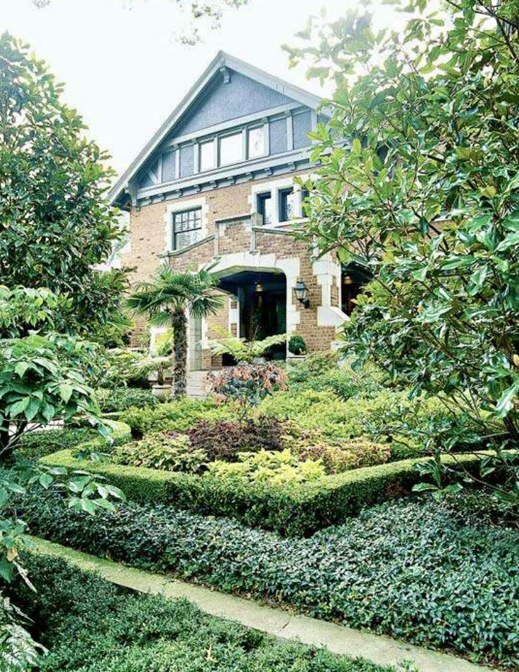 Stone house entrance surrounded by dense hedges, shrubs, and a landscaped garden