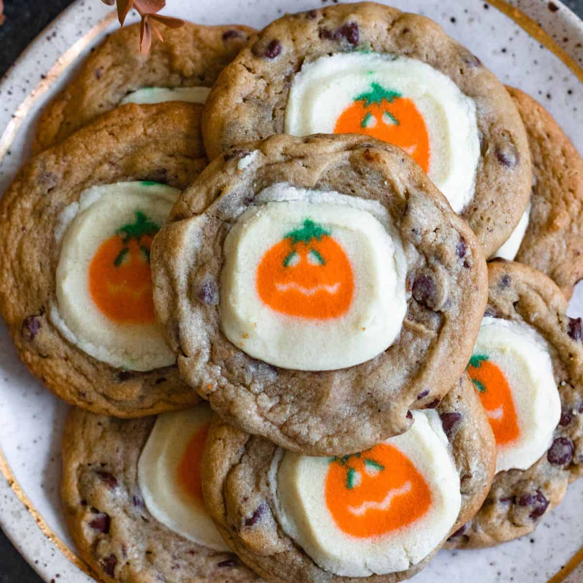 Close-up of chocolate chip cookies with white icing and orange pumpkin decorations on a plate