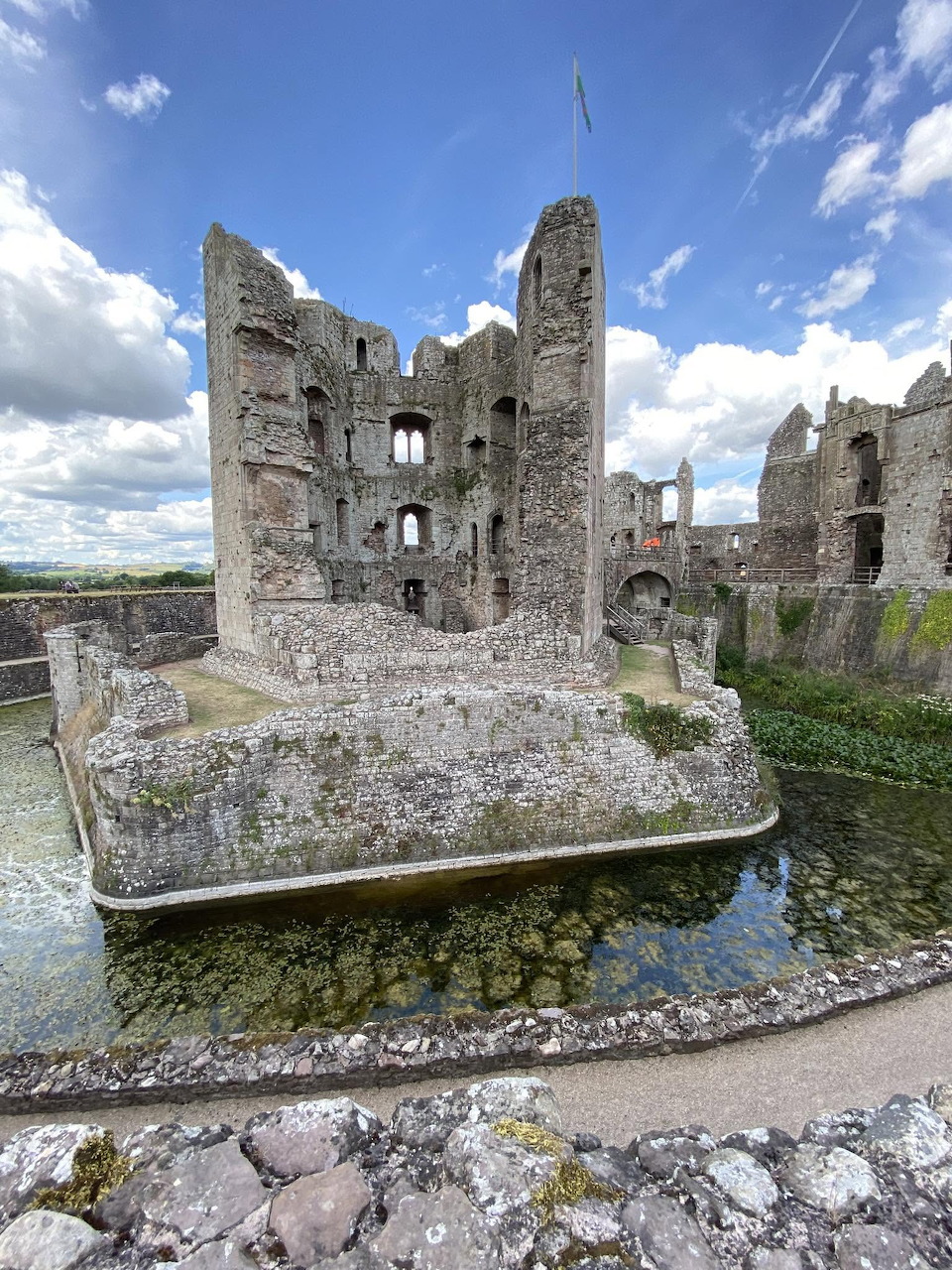 Ruins of Raglan Castle surrounded by a moat under a blue sky