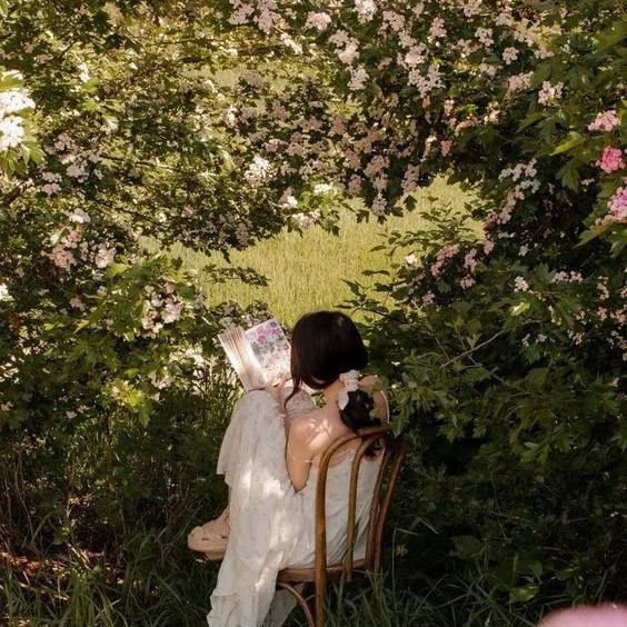Woman in white dress reading a book on a chair in a bloming spring garden