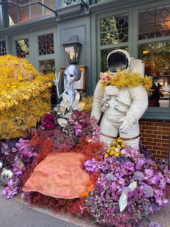 Floral sculptures of astronaut and alien figure covered in yellow, purple, and pink flowers at outdoor display