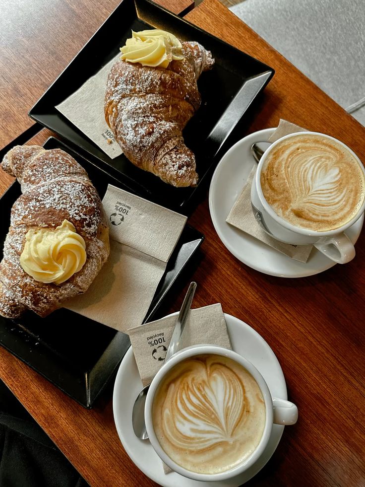 Two cappuccinos with latte art and croissants on wooden tray