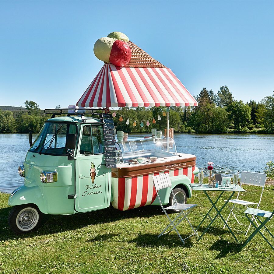 Mint green ice cream truck with striped canopy parked beside a lake on sunny day