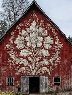 Weathered red barn with a large white floral mural on the front and open central doors
