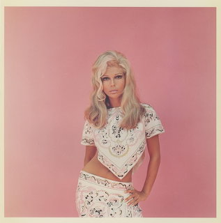 Vintage portrait of Nancy Sinatra in a white patterned outfit against a pink studio background