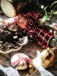 Red metallic toy train with Christmas ornaments, pine branches, candy, and holiday decorations on rustic table