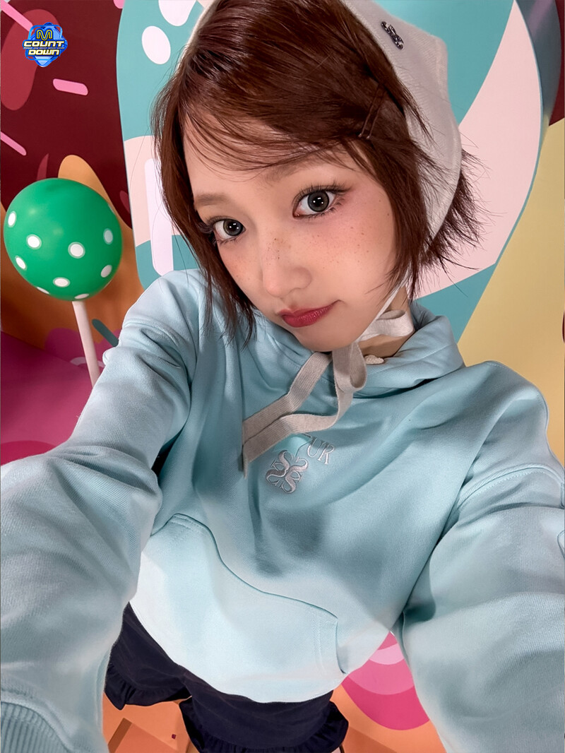Young woman in a light blue hoodie taking a selfie in front of a colorful candy-themed backdrop
